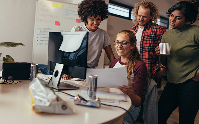 Co-workers gathered around a computer and holding a paper